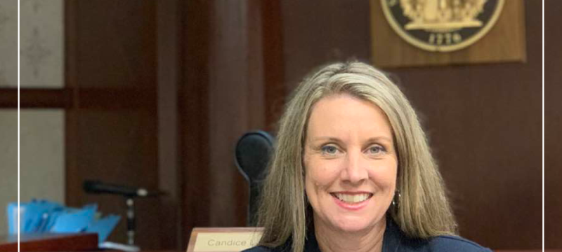 photo of woman in courtroom with state seal and red graphic