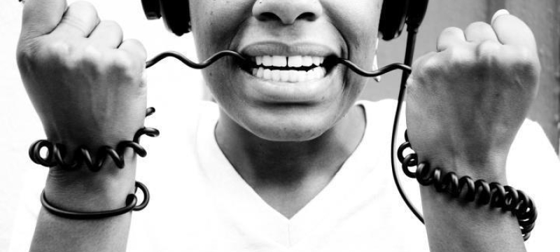 black and white photo of woman wearing headphones with the cord in her teeth