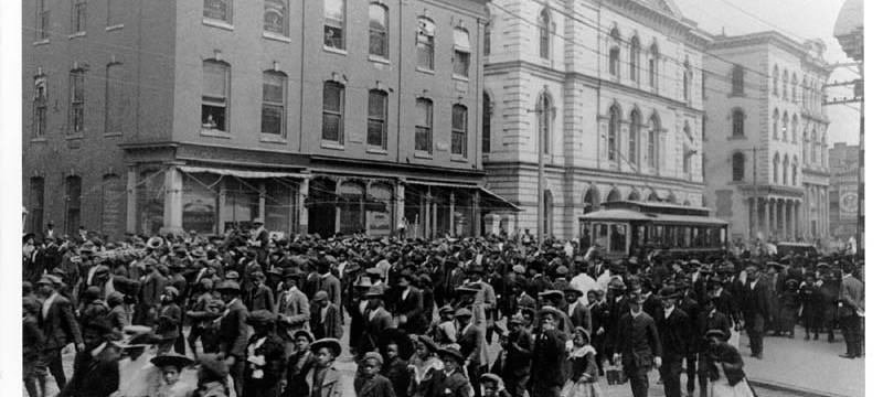 black and white historical photo of people marching on a city street