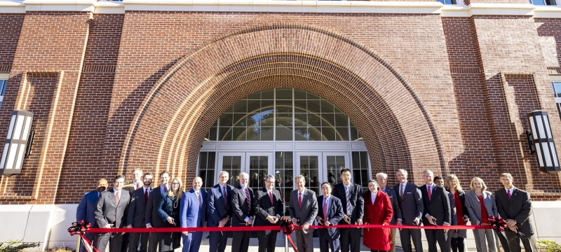 photo of group cutting ribbon in front of building, day