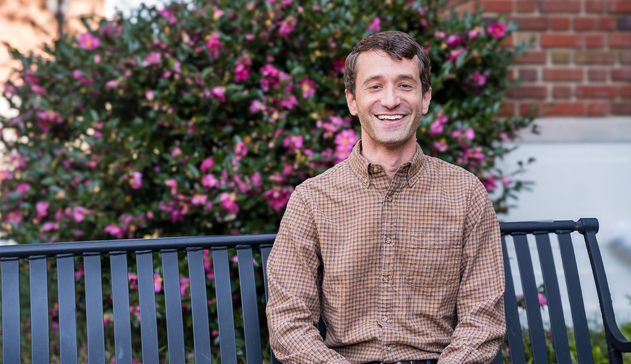Photo of man smiling, sitting on a bench during daytime.