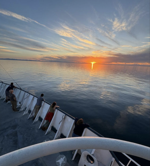 photo of sunset on ocean, with people at rail of ship