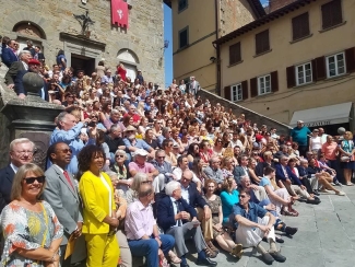 photo of a large group seated on sunny steps of a medieval palace.