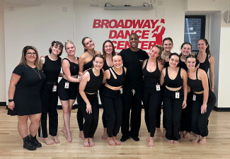 group photo of dancers, sign in background