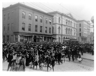 black and white historical photo of people marching on a city street