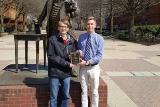 two students with plaque in front of statue