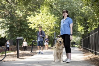 outdoor photo of woman with service dog on sidewalk and other pedestrians.