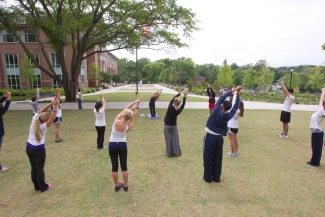 photo of group of people stretching with arms overhead, outdoors