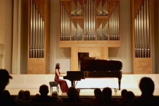 photo of woman in piano performance, with audience silhouette foreground