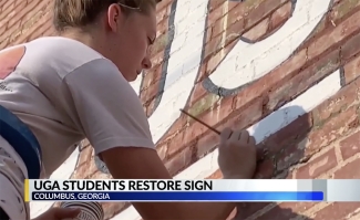 photo of woman painting letters on exterior brick wall