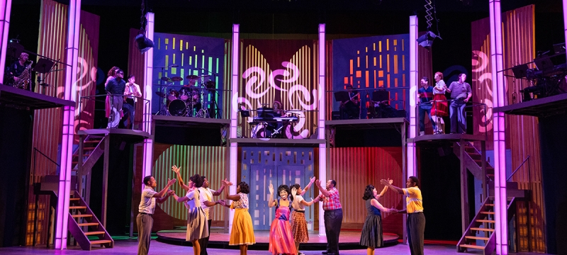 photo of stage play play production with people, lighted columns and steps
