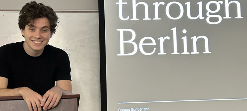 photo of man at lectern, screen with text in background
