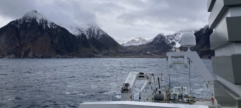 photo of shoreline mountain with clouds, sea and ship in foreground