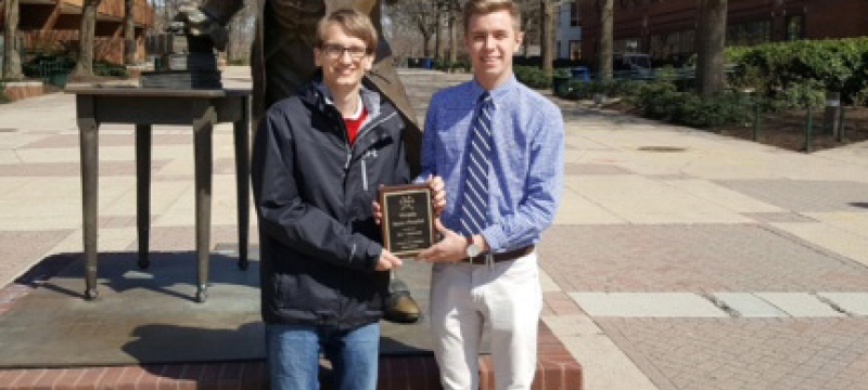 two students with plaque in front of statue