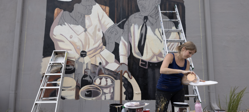 photo of woman mixing paint with mural, ladders, and paint cans