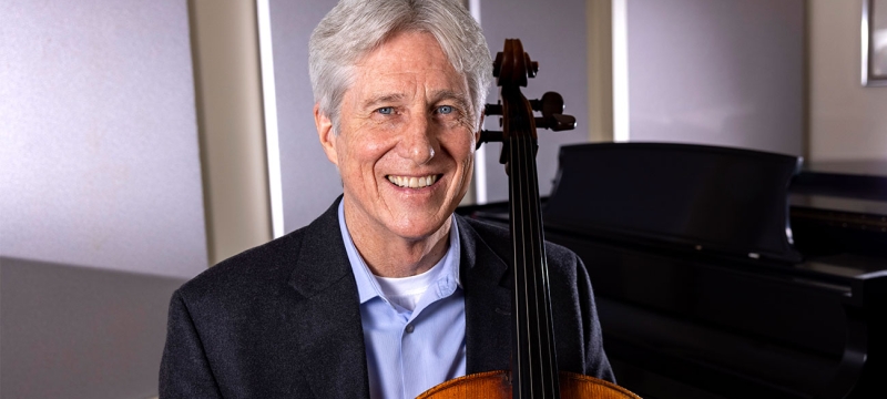 photo of man with cello, piano in background