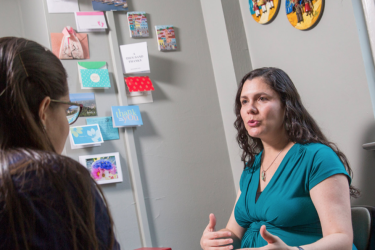 Graduate student Lunara Goncalves interacts with professor Cecilia Rodrigues inside an office.