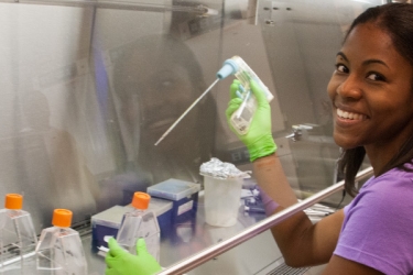 A female biochemistry student works in a lab with chemicals under a ventilator