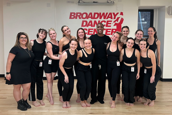 group photo of dancers, sign in background