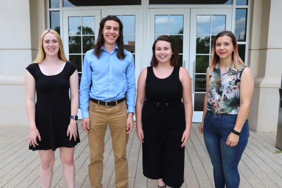 Photo of four scholarship awards winners outside in front of a building