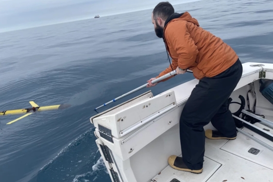 photo of man on boat in ocean with tool reaching for drone in water