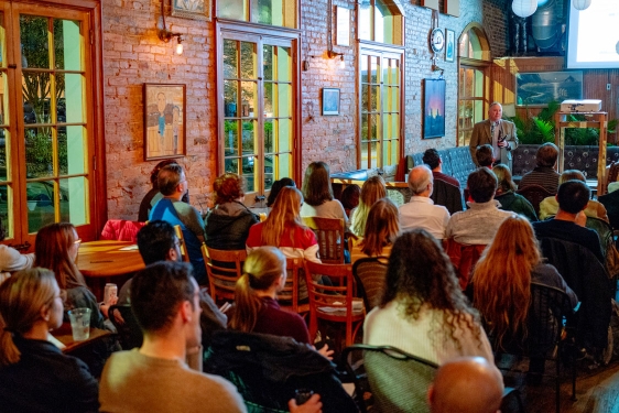 photo of man speaking to seated crowd in a coffee house