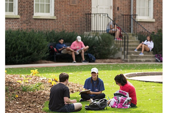students sitting ton the ground in front of brick building