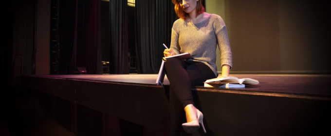 photo of woman sitting on stage with book and pen
