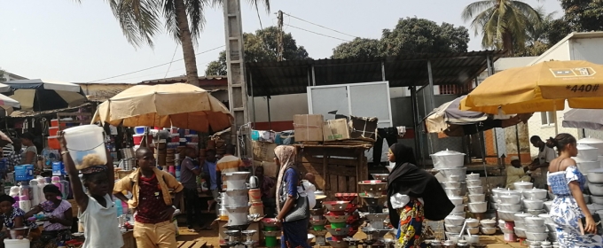 Photo of outdoor marketplace with goods, umbrellas, people and palm trees