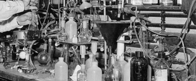black white photo of beakers and test tubes, arms of a man