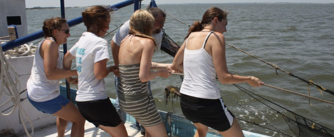 photo of four women pulling rope line on boat