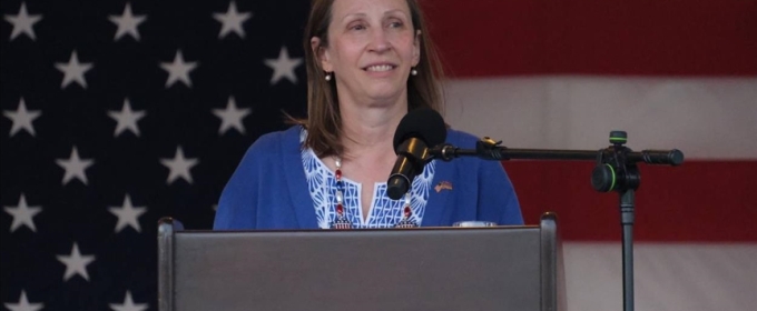 photo of woman at podium, American flag in background